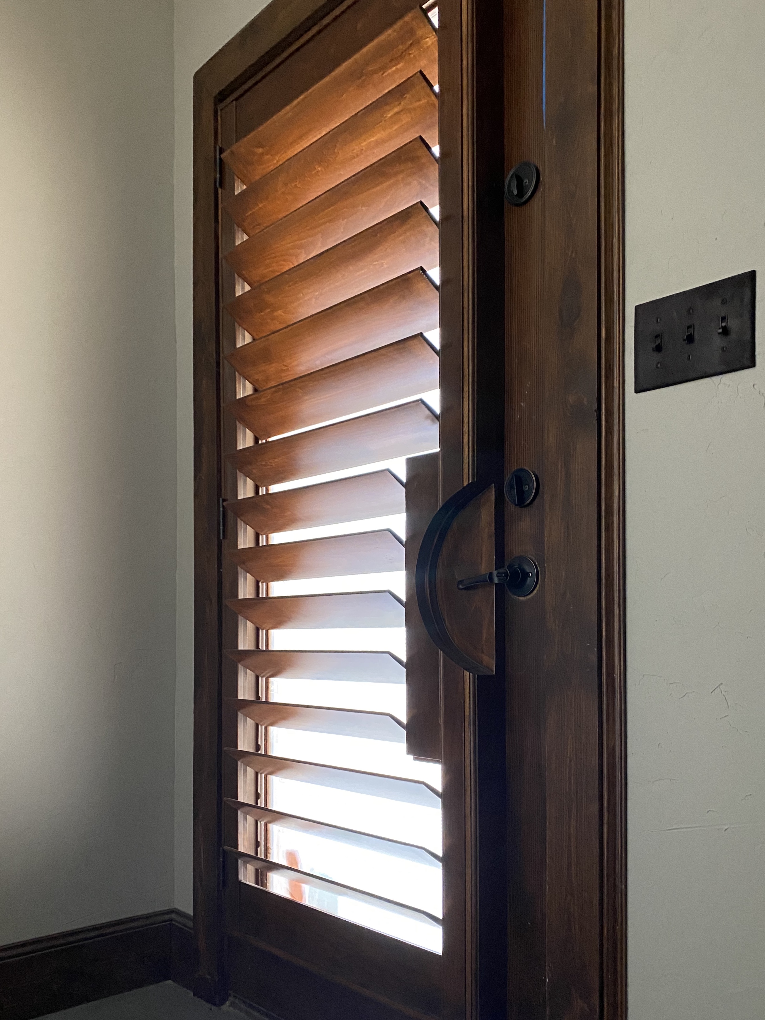 Dark wood shutter blinds on entry door with backlit detail in Decatur TX home
