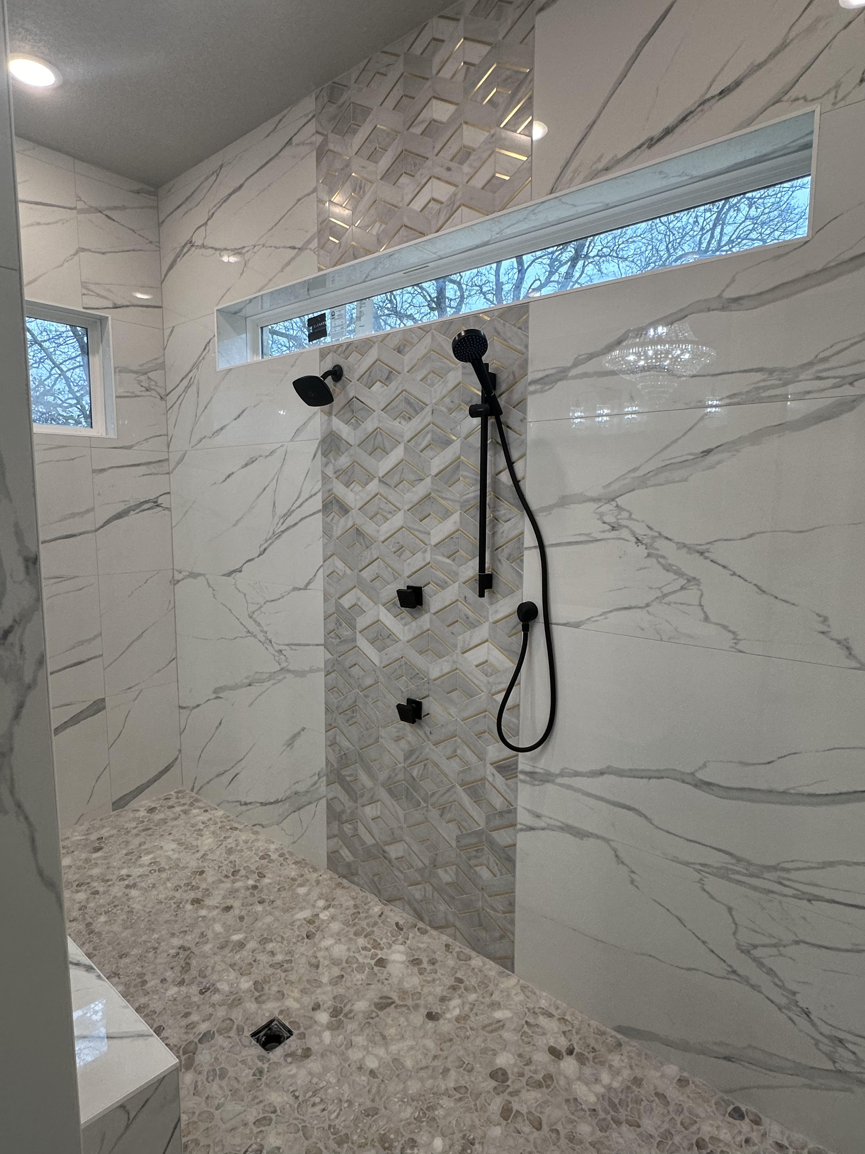 Walk-in shower with marble-look large format tiles, pebble floor, and custom niche installation