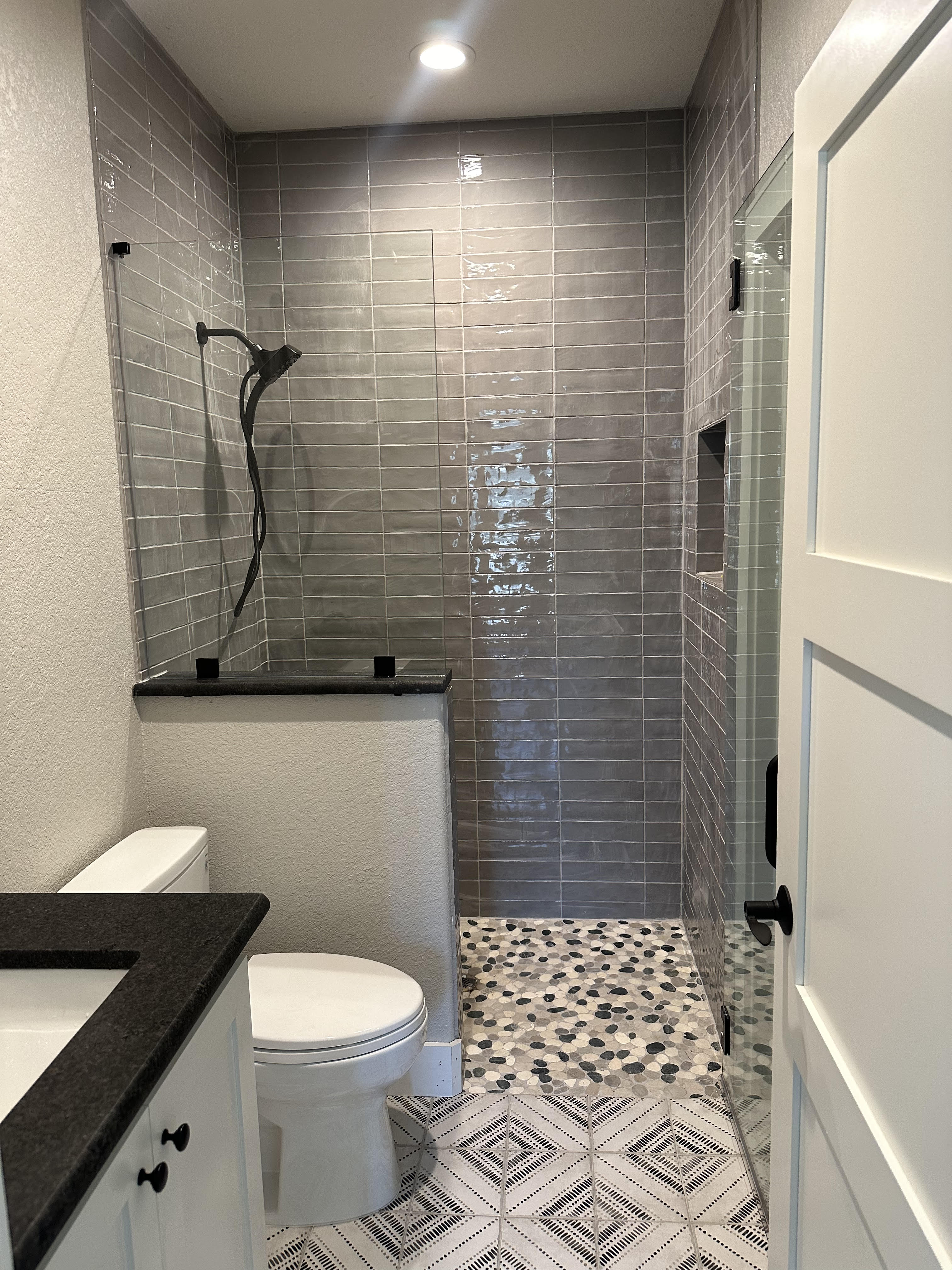 Walk-in shower with dark green glossy subway tile walls and hex penny tile floor with matte black fixtures
